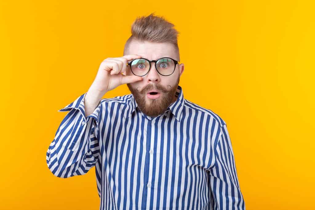 Hombre sorprendido ajustándose las gafas frente a un fondo amarillo, representando confianza y seguridad en préstamos con joyas en Infoprestamojoyas.